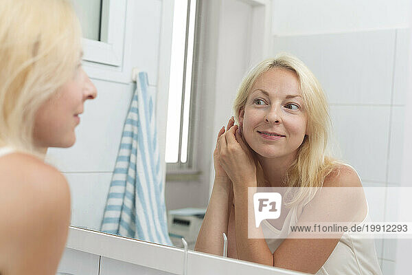 Smiling woman getting dressed looking in mirror at home