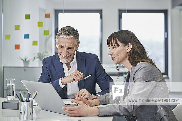 Happy senior businessman discussing with colleague over laptop
