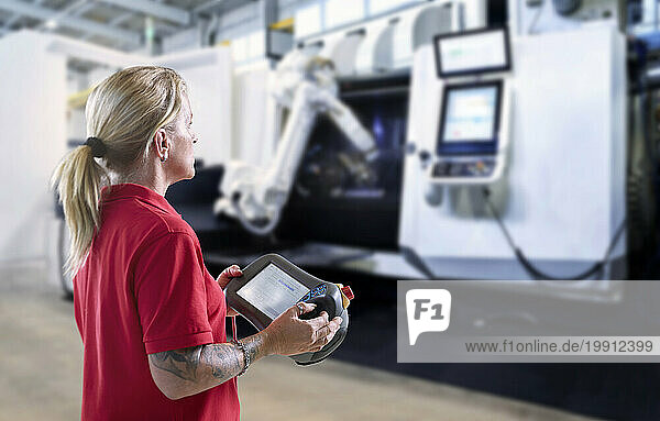 Technician operating robotic arm and machine through tablet PC in factory