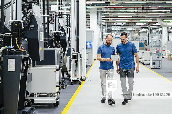Two colleagues walking and sharing digital tablet in a factory