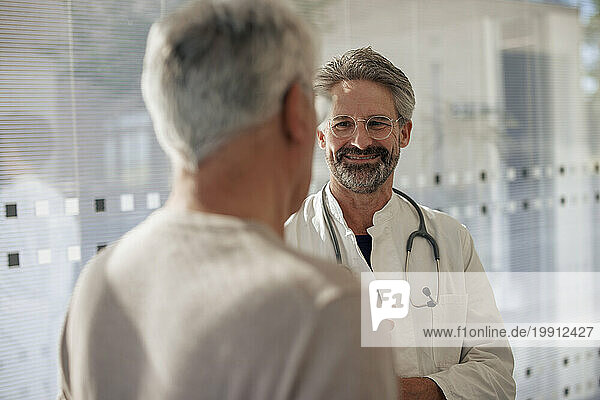 Smiling senior doctor talking to man in hospital