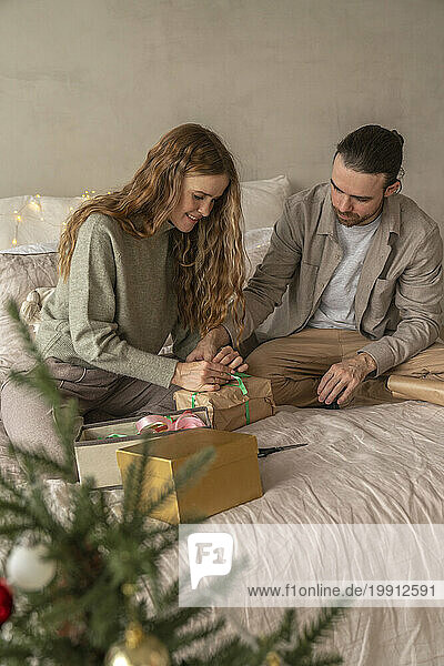 Couple tying ribbon on Christmas present at home