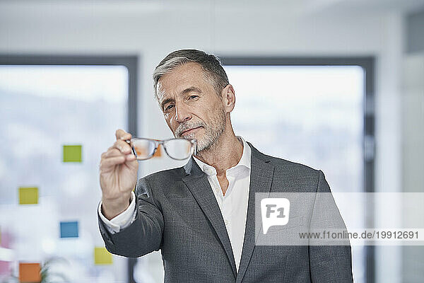 Senior businessman holding eyeglasses and standing in office