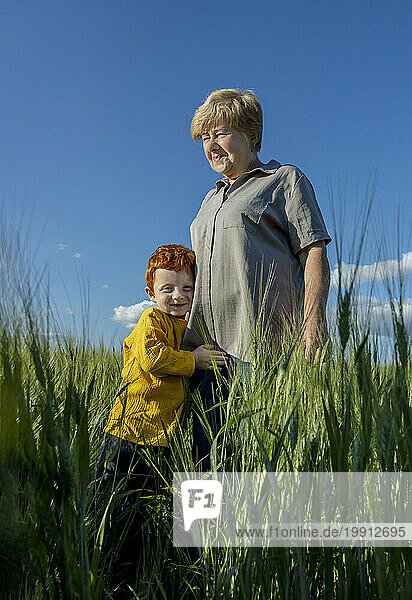 Smiling boy embracing grandmother standing in field