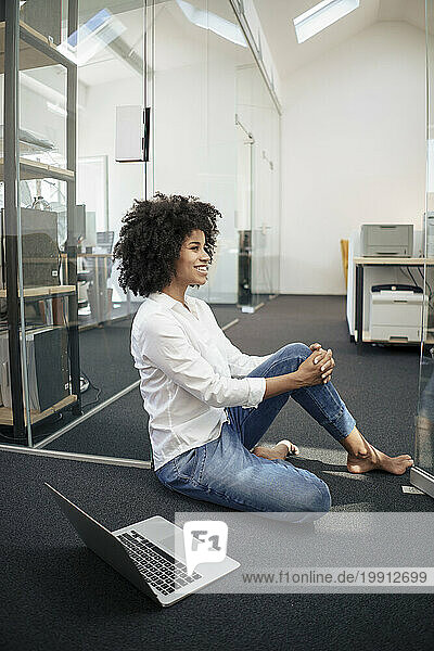 Businesswoman with laptop sitting at doorway in office