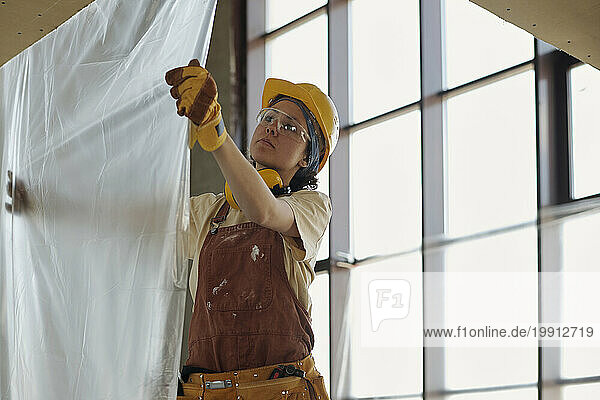 Young construction worker hanging plastic foil at site