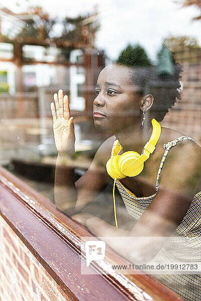 Young woman with headphones around neck looking through window