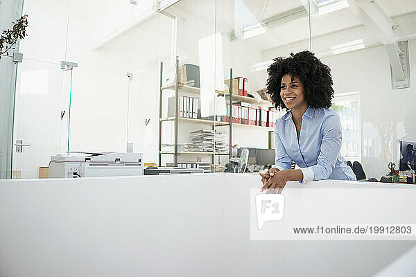 Smiling young businesswoman leaning at office
