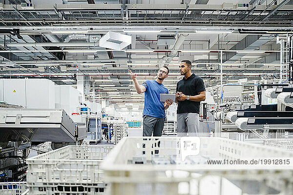 Two colleagues with digital tablet talking in a factory