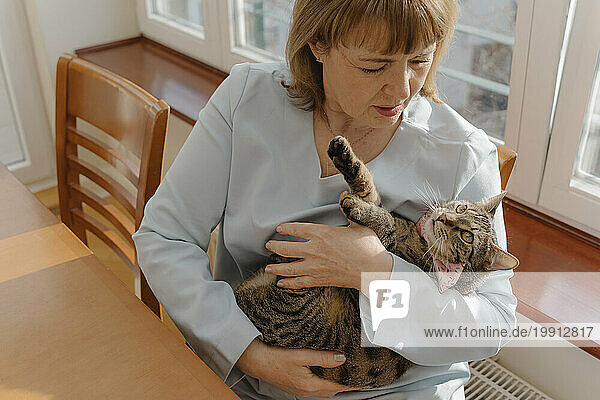 Senior woman embracing cat in arms at home