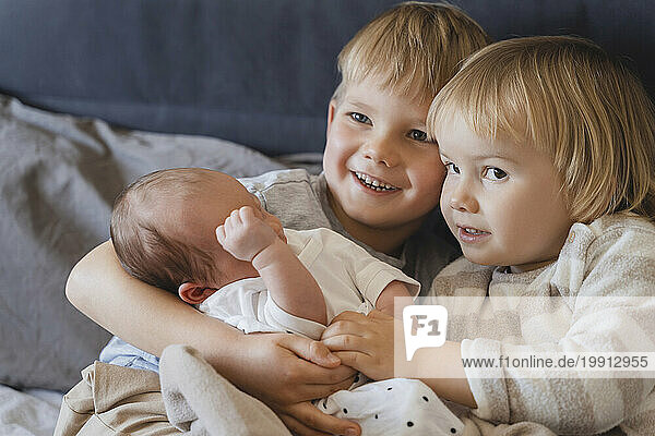 Siblings holding baby boy in arms at home