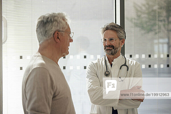 Smiling senior doctor talking to man near glass