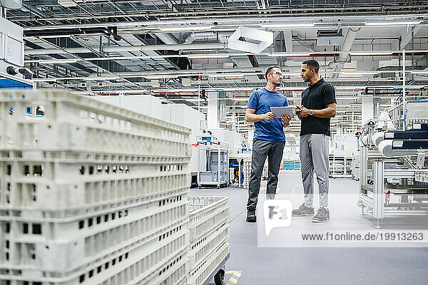 Two colleagues with digital tablet talking in a factory