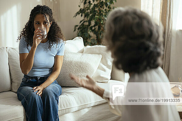 Woman drinking water and having therapy session with psychotherapist at home