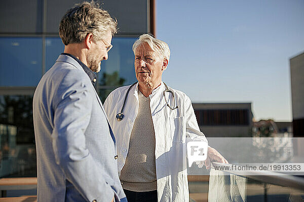 Doctor talking to man near railing on sunny day