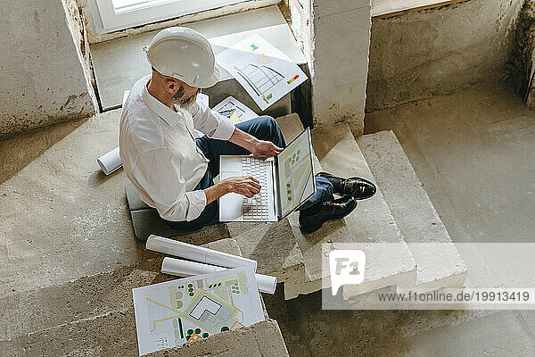 Architect examining blueprint on laptop at site