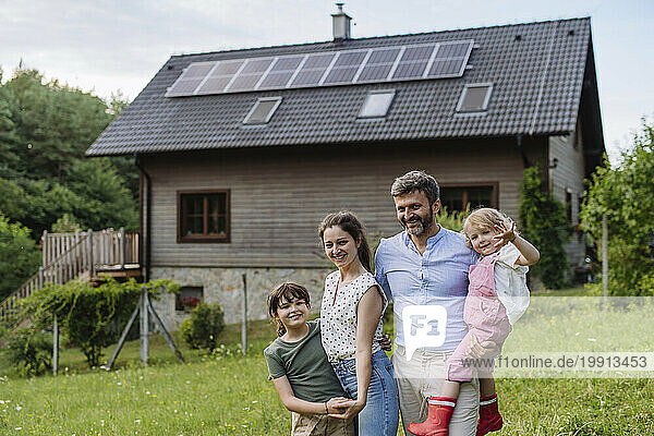 Happy family standing in front their family house with solar panels on the roof