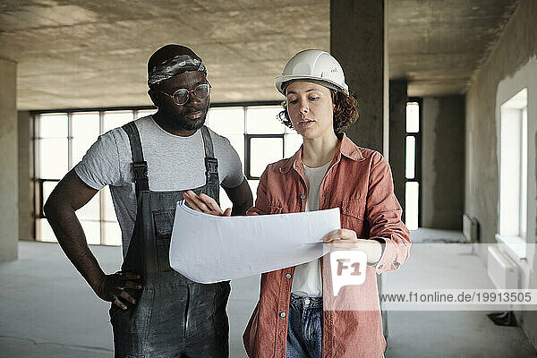 Engineer having discussion over blueprint with construction worker at site