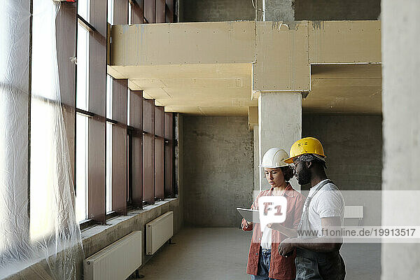 Engineer using tablet PC and discussing with coworker at construction site