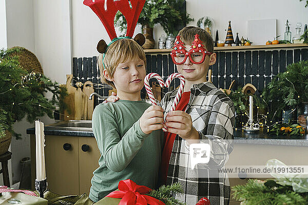 Brothers making heart shape from candy cane in kitchen at home