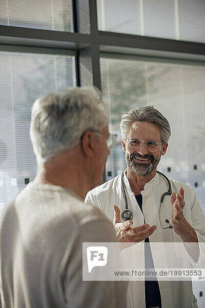 Happy senior doctor discussing with man near glass window in hospital