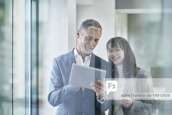 Smiling businessman discussing over tablet PC with colleague in office