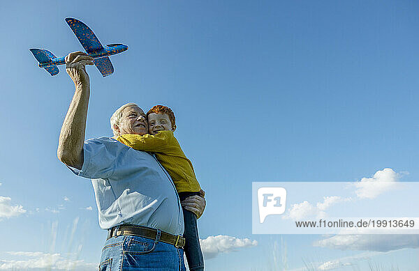 Grandfather and grandson playing with toy airplane under sky