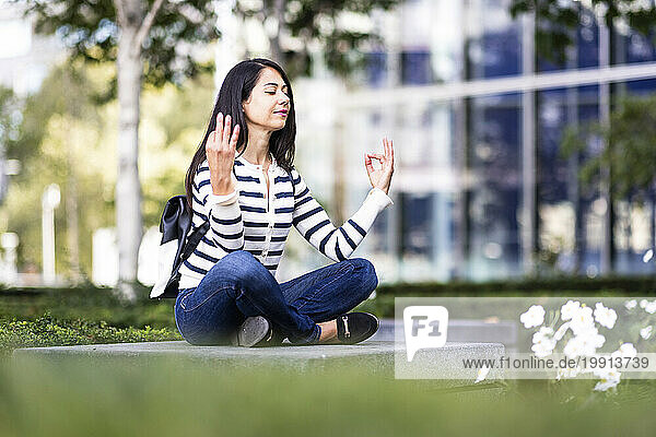 Smiling woman meditating on concrete seat in park