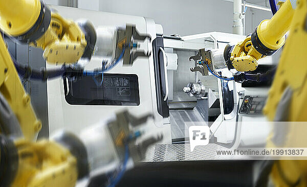 Yellow robotic arms with machinery in factory