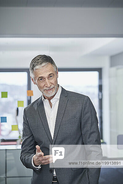 Smiling senior businessman gesturing and standing in office