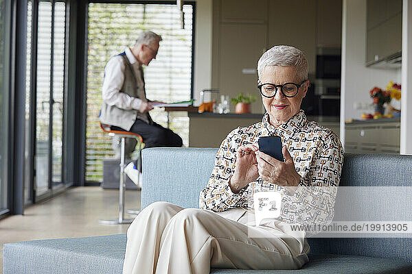 Senior woman sitting on couch at home using mobile phone