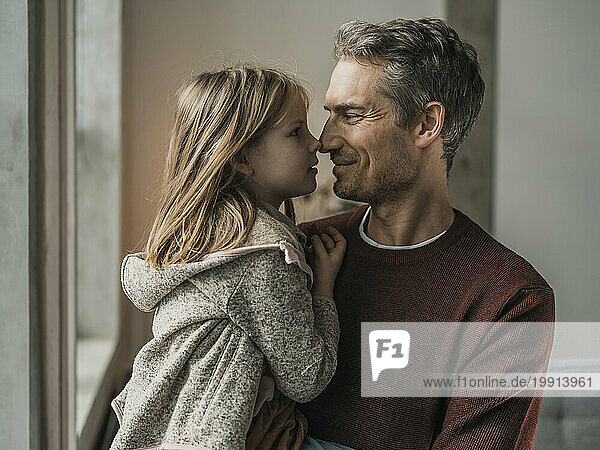 Smiling father rubbing noses with daughter at home