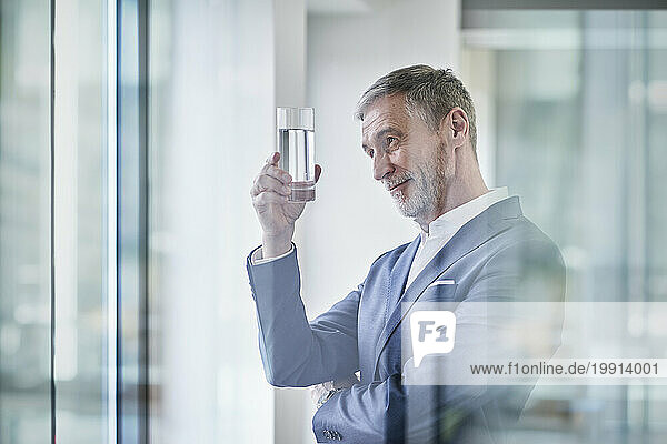 Smiling businessman examining glass of water in office