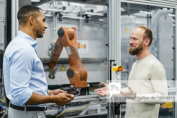 Employee and businessman talking at industrial robot in a factory
