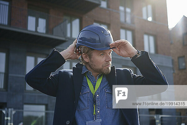 Architect adjusting hardhat in front of buildings on sunny day