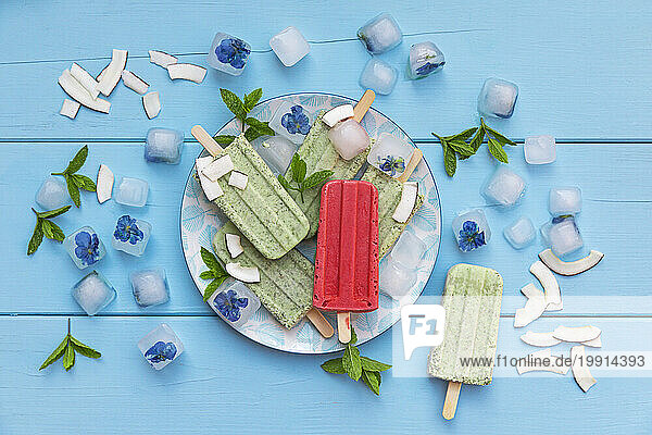 Red strawberry popsicle on plate with green mint and coconut ones