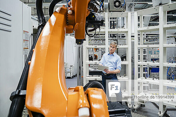 Businessman using digital tablet at industrial robot in a factory