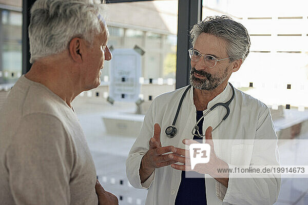 Senior doctor gesturing and explaining to man near glass window