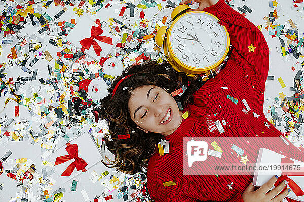 Happy girl lying on confetti with clock and gift boxes
