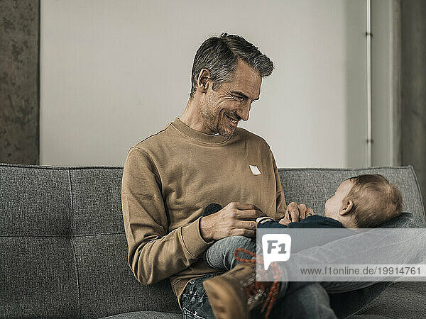 Happy father playing with baby boy on sofa at home