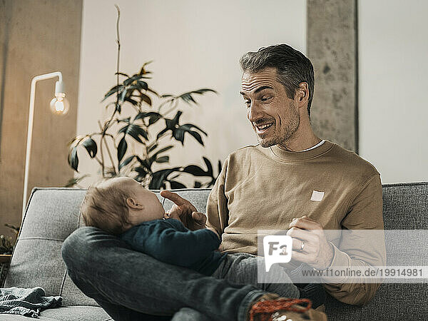 Happy father playing with baby boy in living room at home