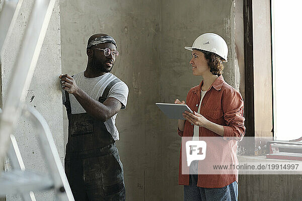 Smiling engineer holding tablet PC and having discussion with colleague at site
