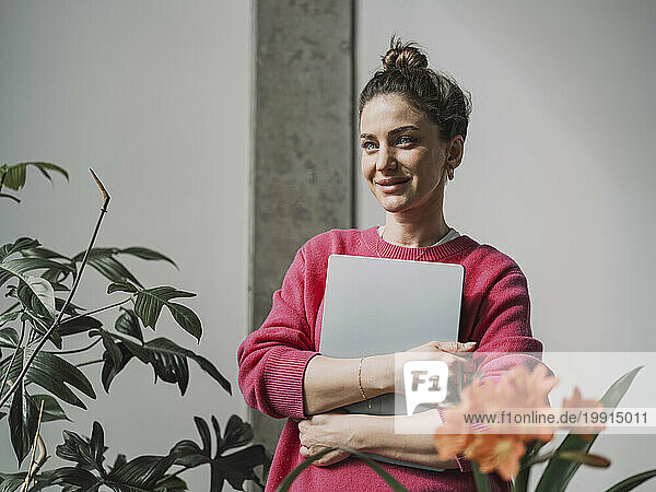 Smiling beautiful businesswoman holding laptop in front of wall