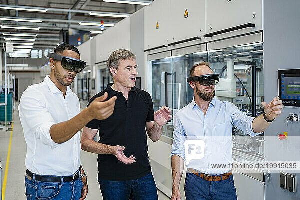 Two technicians wearing augmented reality glasses in a factory and interacting with colleague