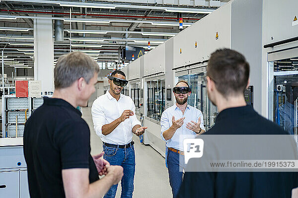 Colleagues watching two technicians wearing augmented reality glasses in a factory