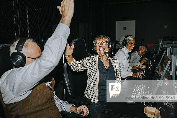 Happy senior couple giving high-five by male and female friends while winning video game at gaming lounge