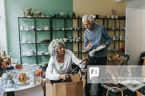 Elderly female entrepreneur analyzing fishing rod with male colleague at antique shop