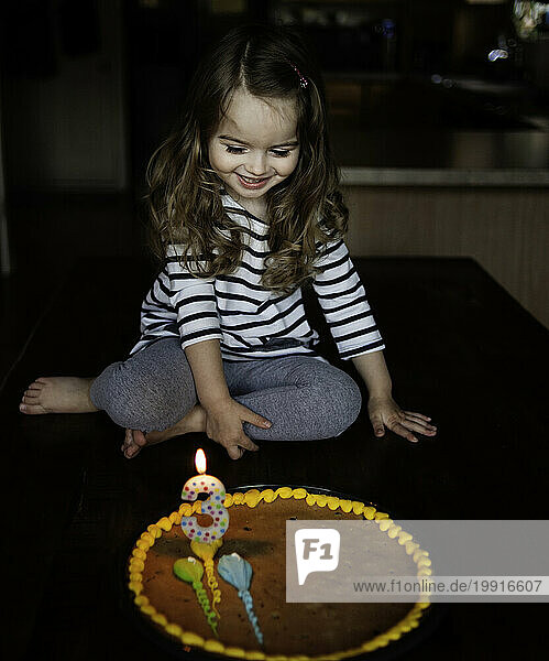 Happy little girl looking at birthday cake in kitchen