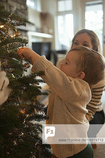 Mother and toddler happily decorating family Christmas tree