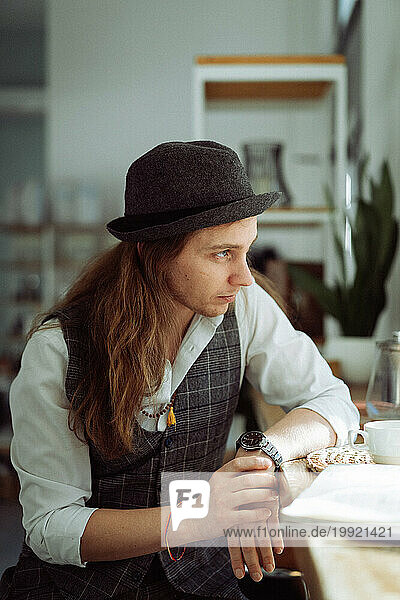 Young man caucasian with long blond hair wearing a hat in a cafe.